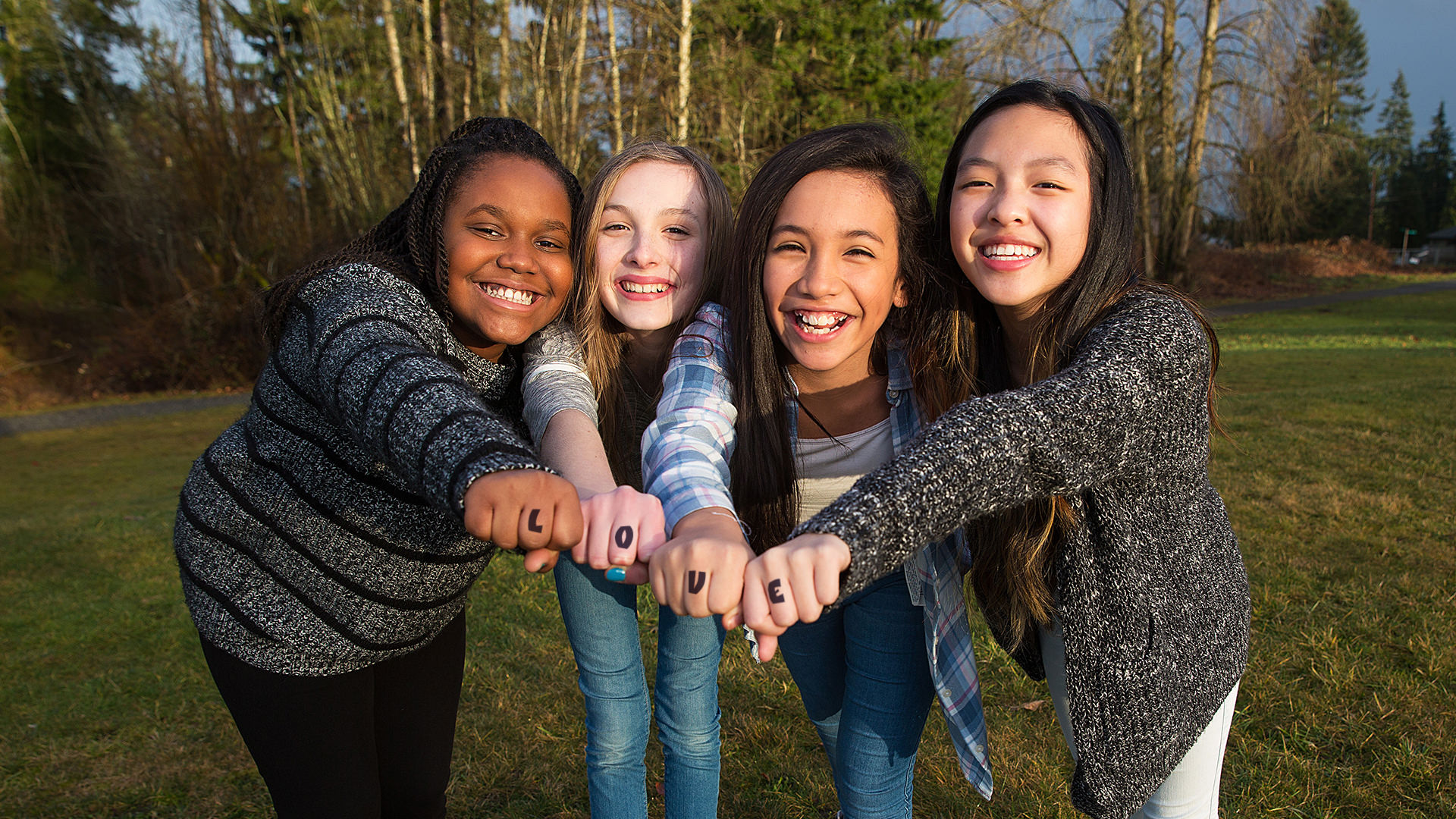 Group of four kids making a unified fist to demonstrate girl pow Teen girls with the word LOVE written on their hands